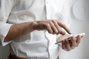 Man in a white button up shirt tapping on his phone.