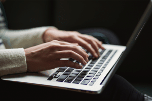 Person typing on their laptop while it sits in their lap.